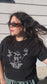 Person wearing a black t-shirt with a white graphic design against a light wooden panel background